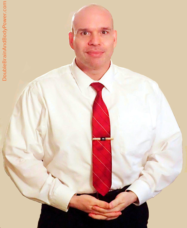 Picture of Mark Cammack wearing a long sleeve white dress shirt, red tie, and black pants. There is a grey background.
